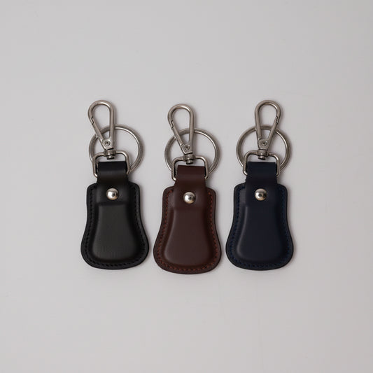 Three small leather keychain fobs with metal key rings and lobster clasps, shown on a plain light background. The fobs are black, dark brown, and black again, with gold-tone hardware.